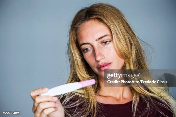 young woman looking at pregnancy test with disappointed expression - infertilidad fotografías e imágenes de stock