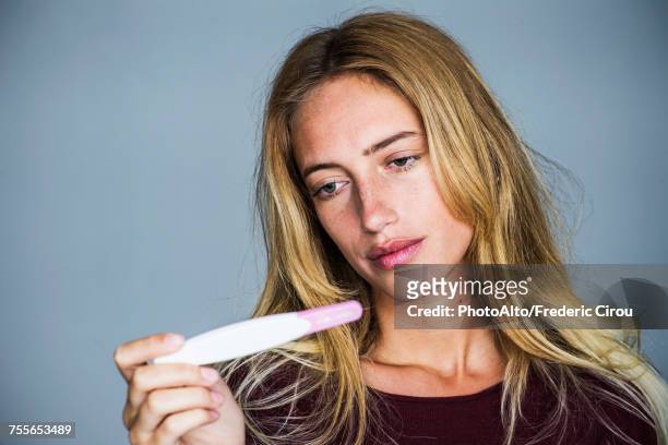 young woman looking at pregnancy test with disappointed expression - infertility stock pictures, royalty-free photos & images