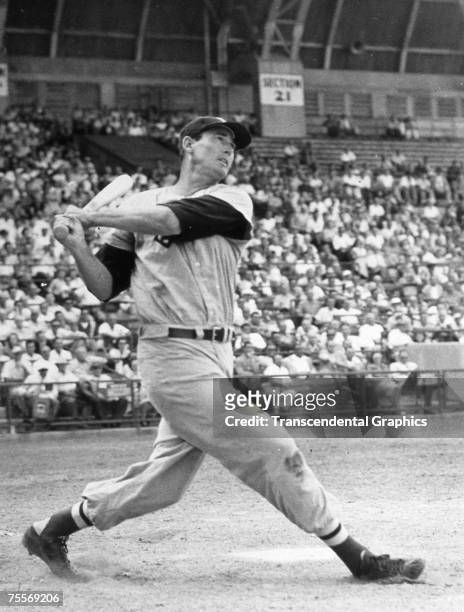 Around 1952, in an unknown ballpark, Ted Williams takes a huge swing before a large crowd.