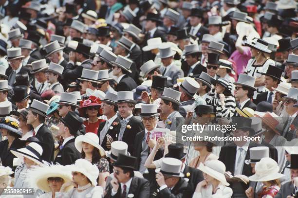 View of a crowd of male and female racing fans and spectators wearing top hats, wide brimmed hats and formal dress as they watch the racing at the...