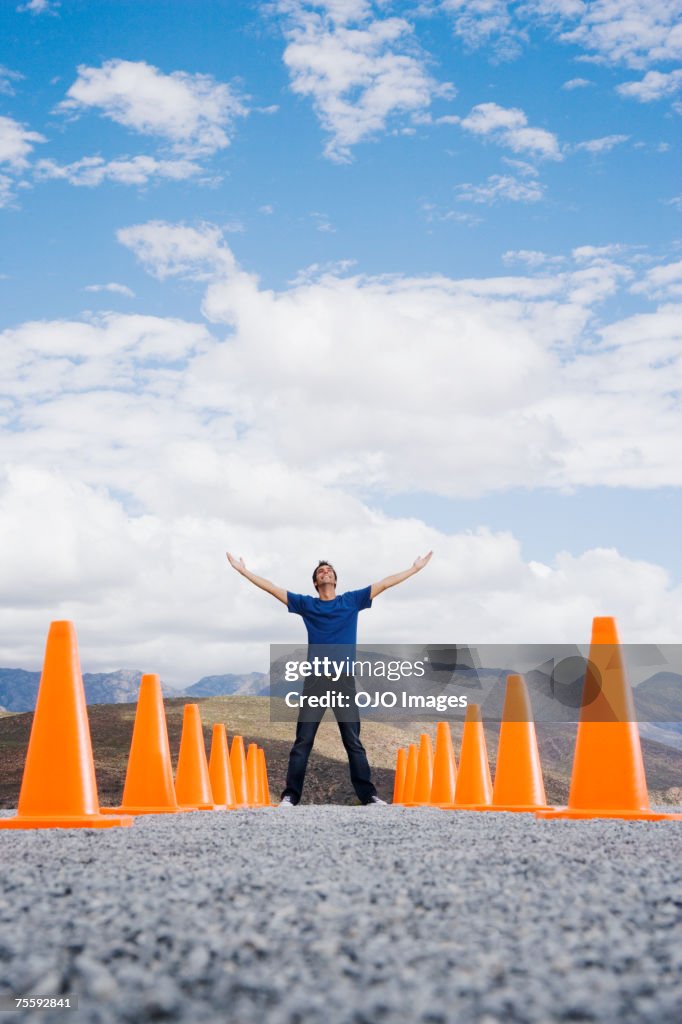 Man with outstretched arms standing in-between two rows of safety cones