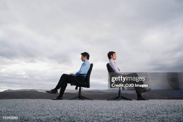 two men sitting in office chairs outdoors with their backs against one another - business confrontation stock pictures, royalty-free photos & images