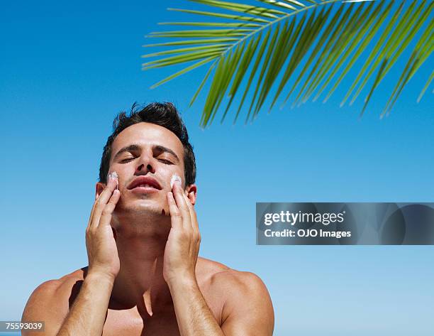 young man applying lotion to face - applying sunscreen stock pictures, royalty-free photos & images