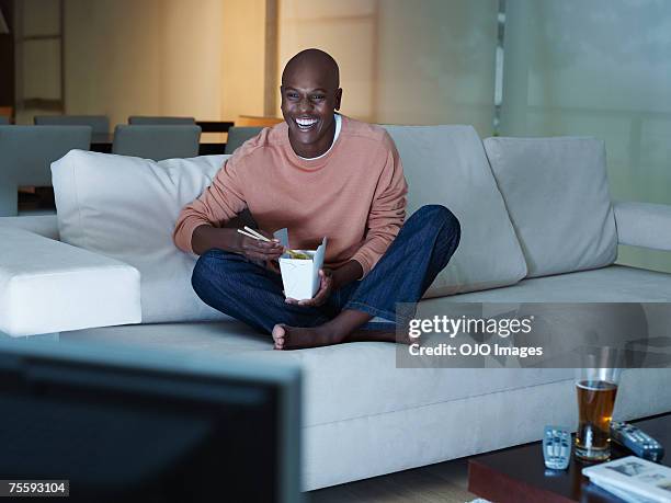 man eating chinese food watching television - african watching tv stock pictures, royalty-free photos & images