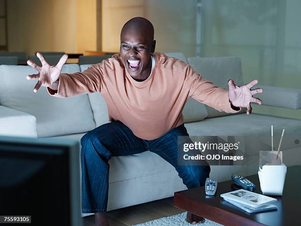 man excitedly watching the television - african american watching tv stock pictures, royalty-free photos & images