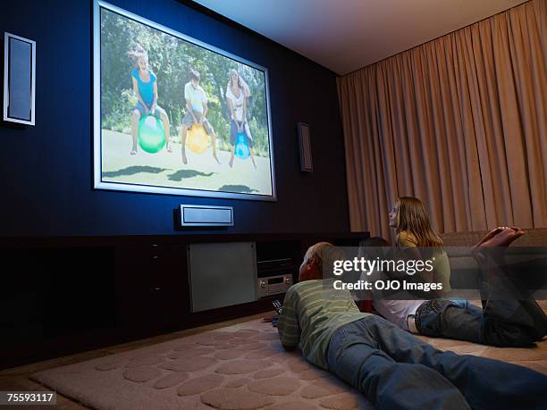 three young kids watching a large wall television - boy at television stockfoto's en -beelden