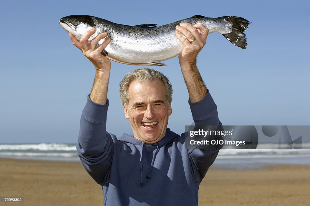 Man holding up a whole fish at the beach