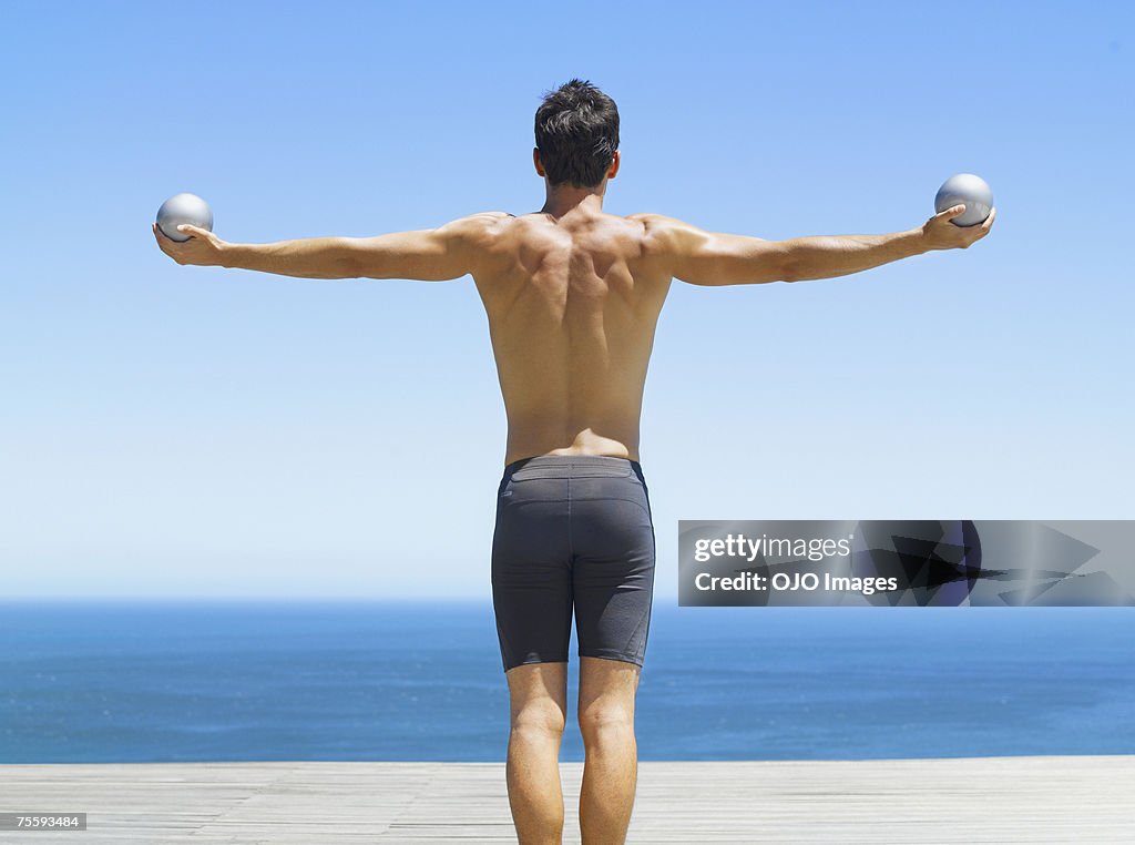 Mann hält zwei kleine Gymnastikbälle mit ausgestreckten Armen