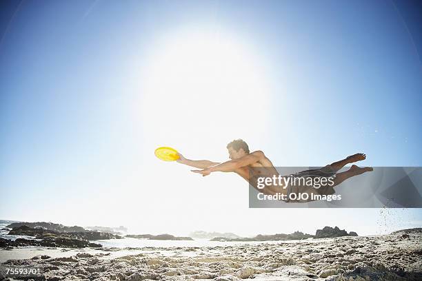 un hombre del salto del a el aire en la playa disfrutando de un disco volador - frisbee fotografías e imágenes de stock