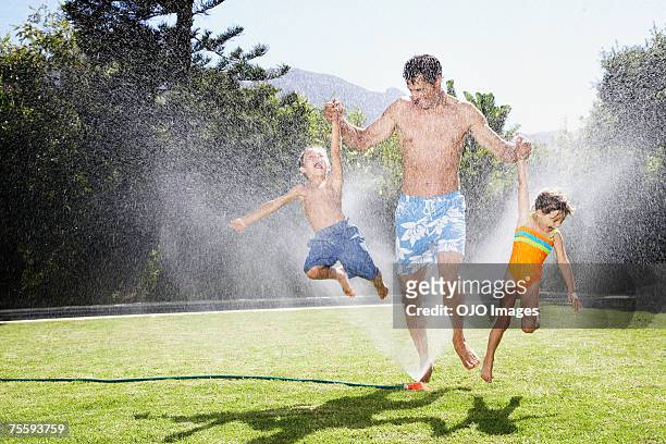 a father playing with his children in a sprinkler - jumping sprinkler stock pictures, royalty-free photos & images