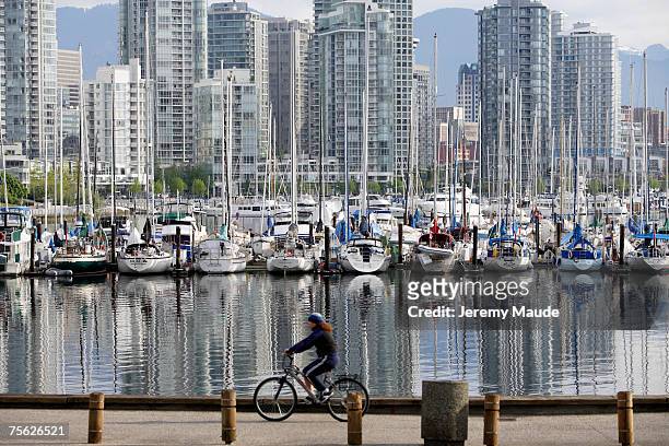 woman cycling along harbour, boats and skyscrapers in background - vancouver train stock pictures, royalty-free photos & images