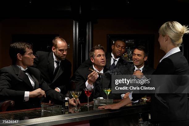 men in dinner jackets drinking cocktails in bar, one holding cigar - tuxedo party stock pictures, royalty-free photos & images