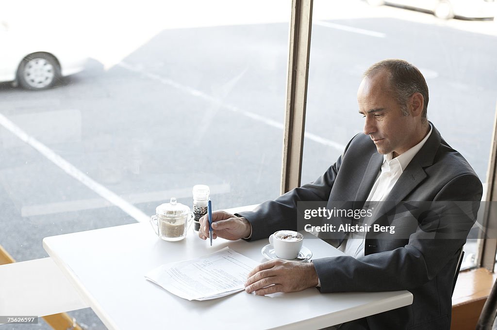 Mid adult business man sitting at cafe table reading documents