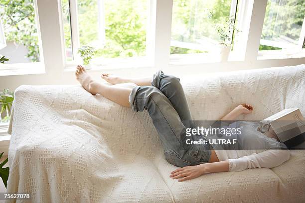 woman sleeping on sofa in living room, book covering face - soffpotatis bildbanksfoton och bilder