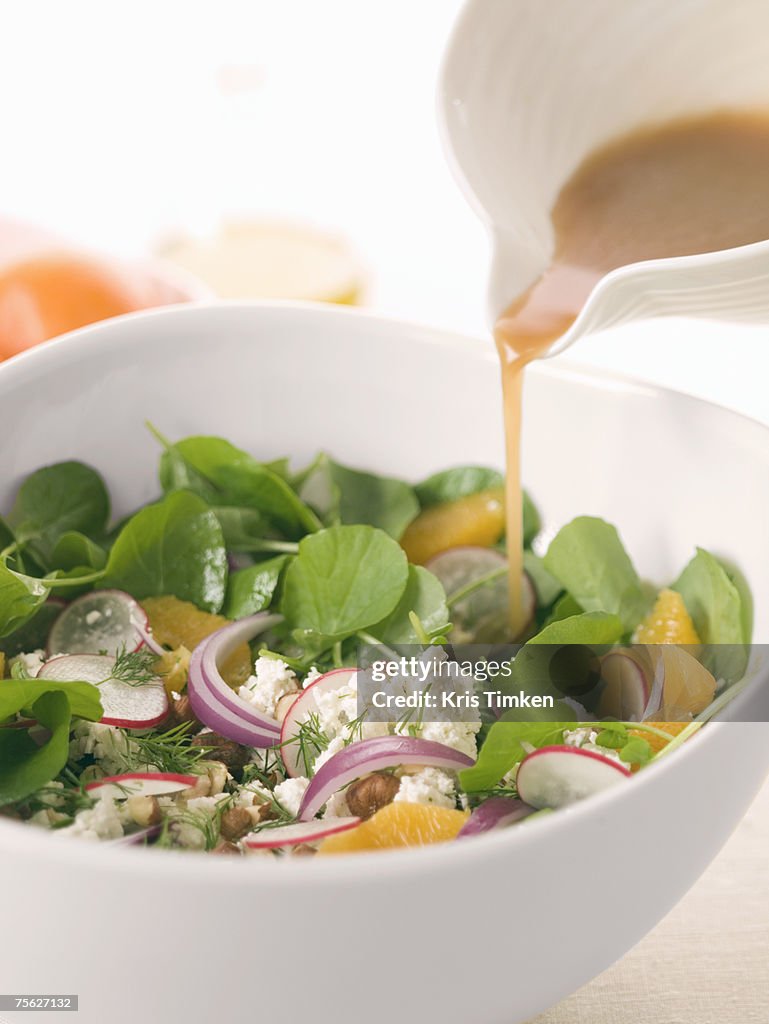 Balsamic dressing being poured on fresh salad in white bowl, close-up