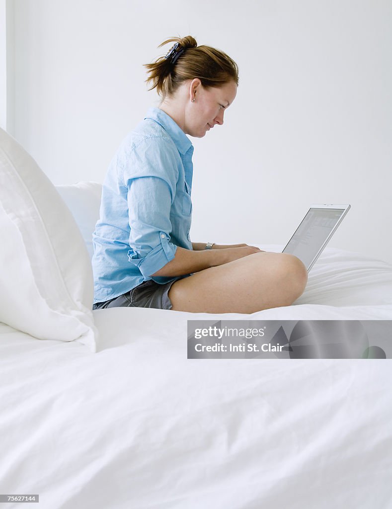 Mature woman sitting on bed using on laptop, side view