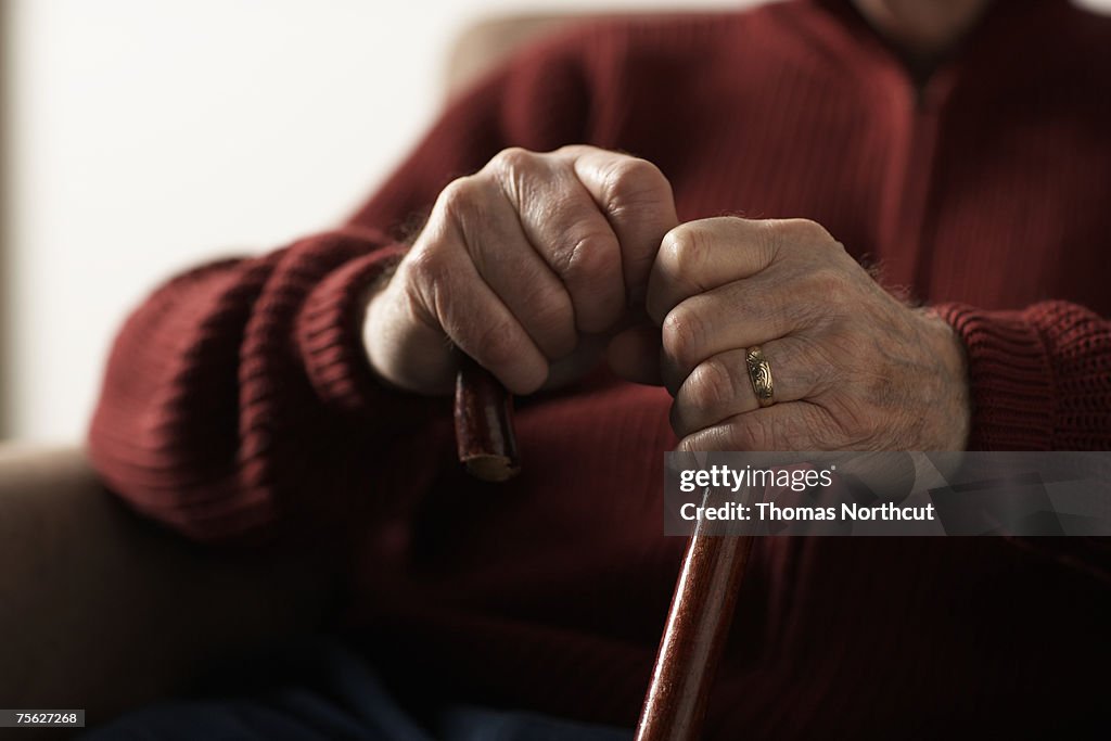 Senior man holding cane, mid section, close-up of hands