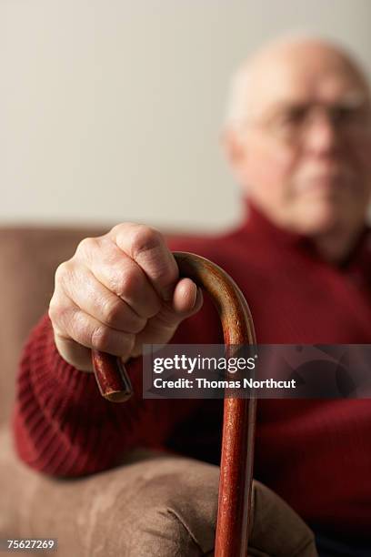 senior man sitting in armchair, holding cane, focus on hand - indecisive stock-fotos und bilder