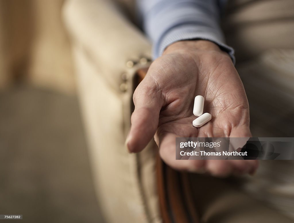 Senior woman holding two pills, close-up of hand