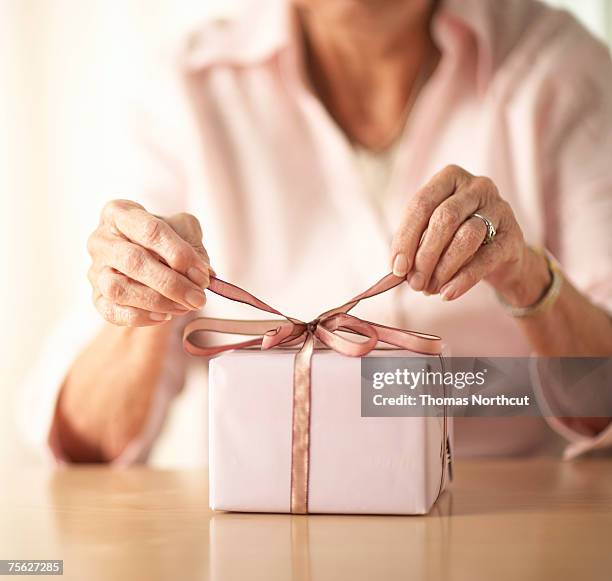 senior woman tying bow on gift, mid section, close-up of hands - candy wrapper stock pictures, royalty-free photos & images