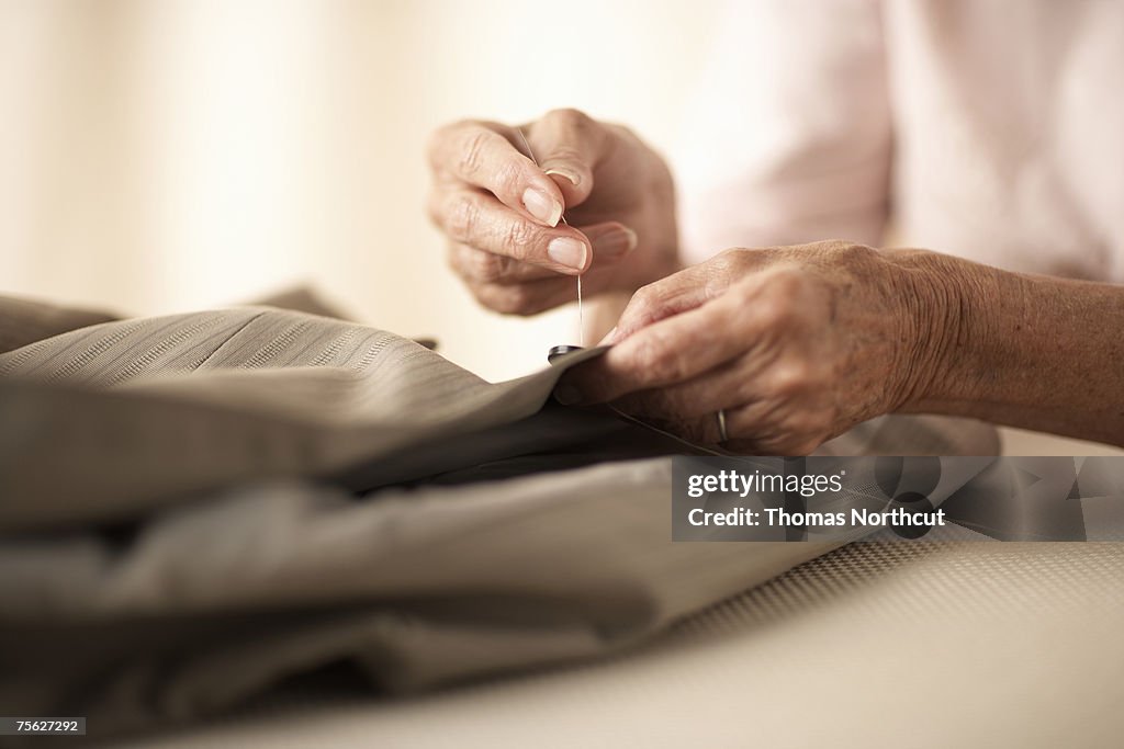 Senior woman sewing button on jacket, close-up of hands