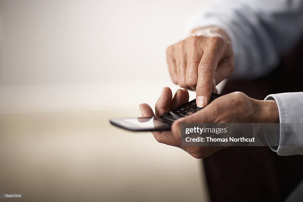 Senior man using mobile phone, close-up of hands