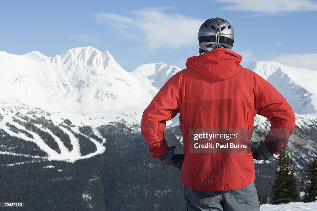 Man in helmet standing against snow-covered mountains, rear view