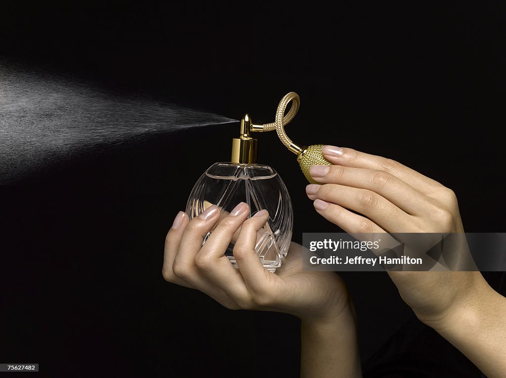 Woman spraying perfume with perfume atomizer, close-up of hands