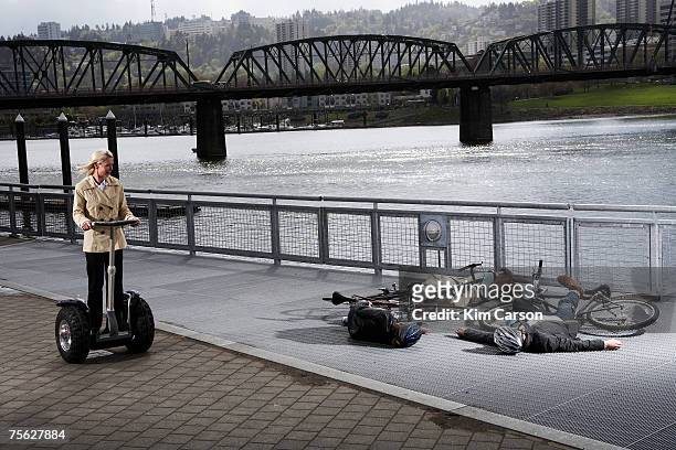 woman on segway riding past two men and woman with bicycles lying on pavement by river - unconscious stock pictures, royalty-free photos & images