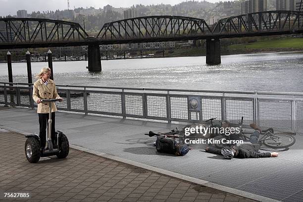 woman on segway riding past two men and woman with bicycles lying on pavement by river - traffic accident stock-fotos und bilder