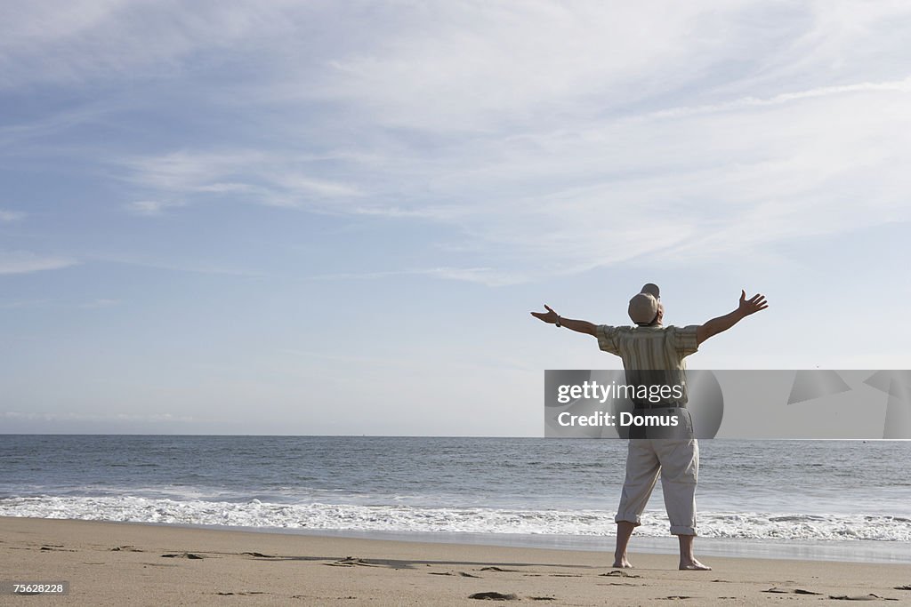 Man with arms outstretched on beach, facing ocean, rear view