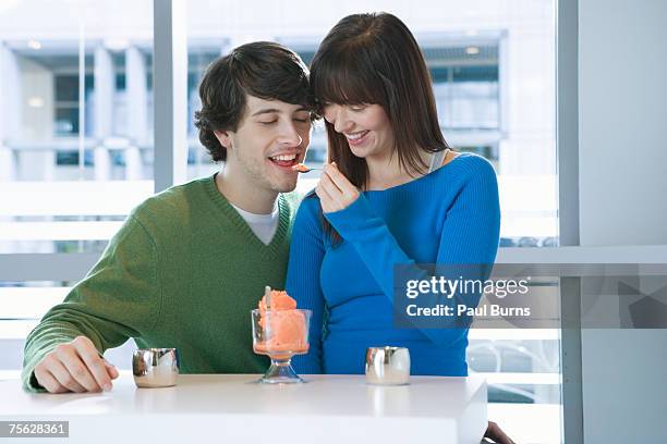 young man and woman sitting at cafe, woman feeding boyfriend orange sorbet, laughing - orange sorbet stock pictures, royalty-free photos & images