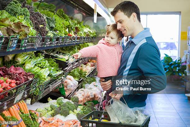 man carrying girl (18-21 months) and basket in supermarket, half length - produce aisle photos et images de collection