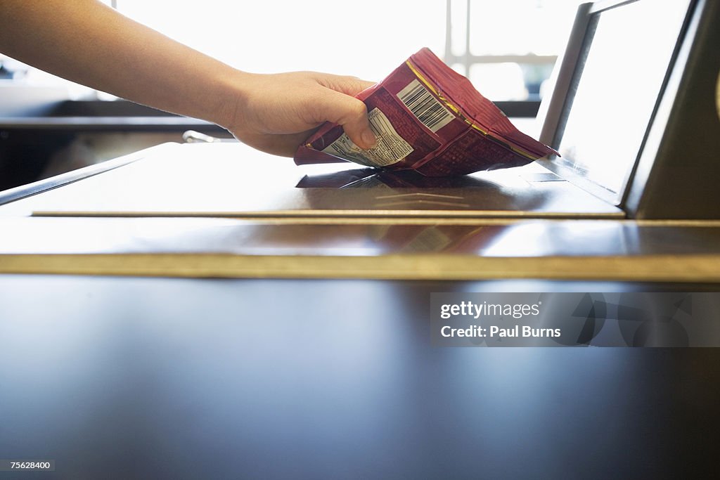 Sales clerk scanning packet at till, close-up of hand