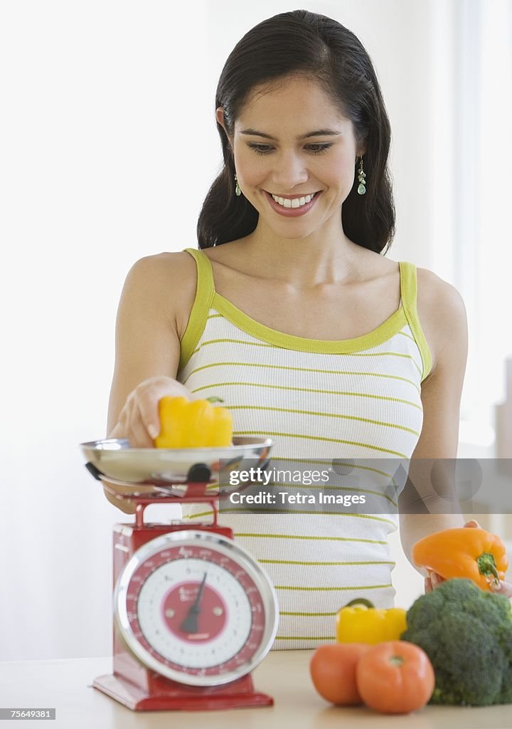 Woman weighing vegetables in kitchen