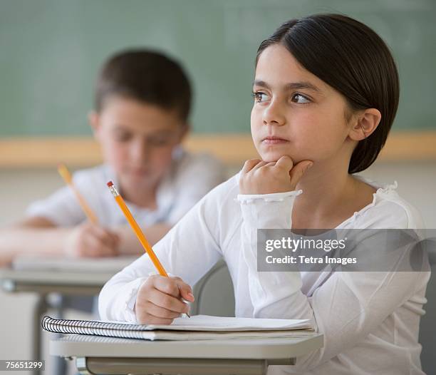 girl thinking at desk in classroom - niños pensando fotografías e imágenes de stock