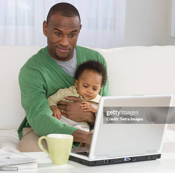 father holding baby and typing on laptop - family on couch with mugs stock pictures, royalty-free photos & images