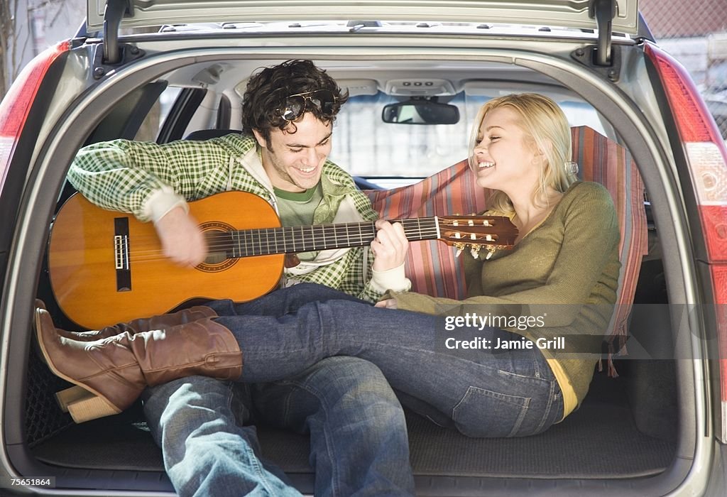 Couple sitting in back of car with guitar