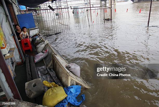 Woman and her child sit in front of a store inundated by floodwaters on the shores of the Yangtze River, on July 25, 2007 in Wuhan of Hubei Province,...