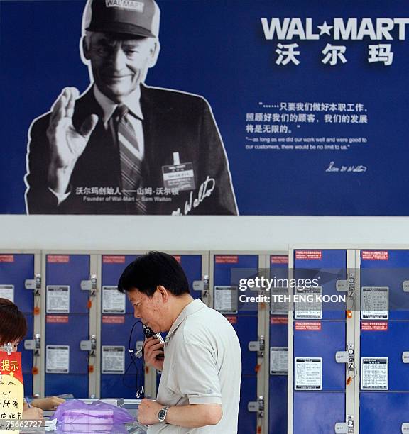 Shopper stands near a poster of Sam Walton, founder of Wal-Mart, at a Wal-Mart in Beijing, 26 July 2007. US retail giant Wal-Mart Stores Inc said on...