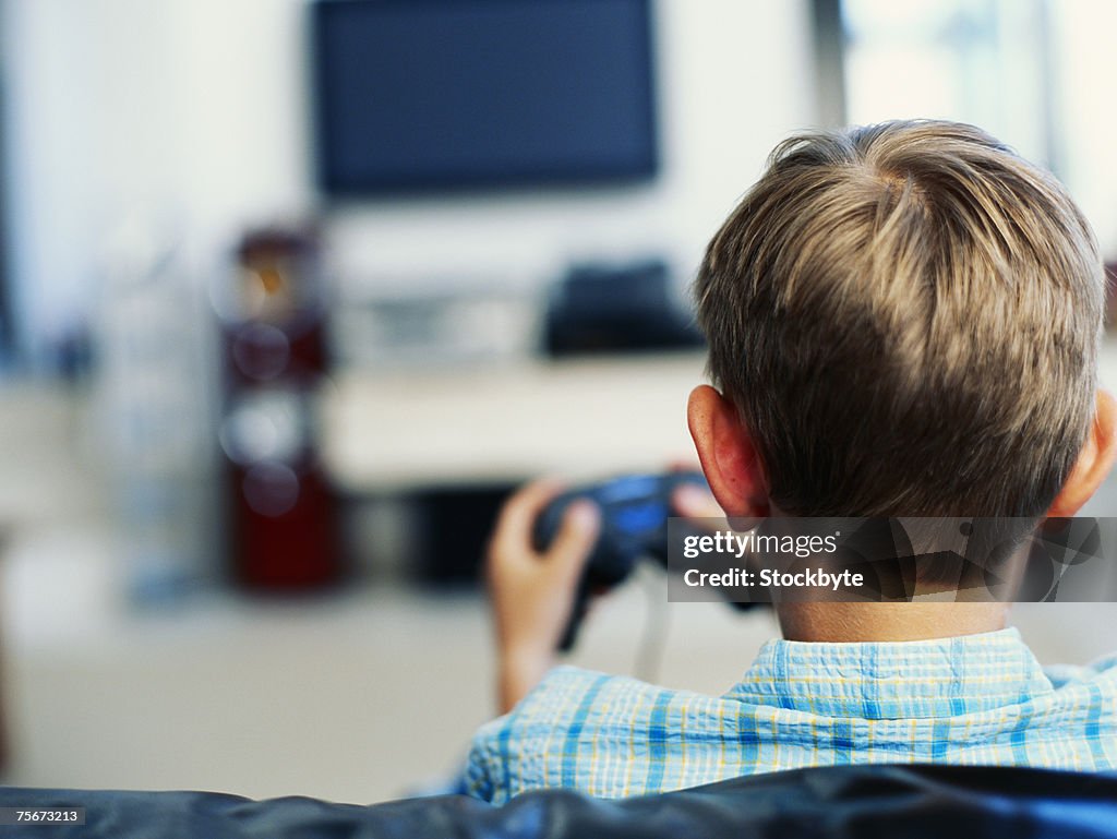 Boy (6-9) sitting on sofa playing video game, rear view