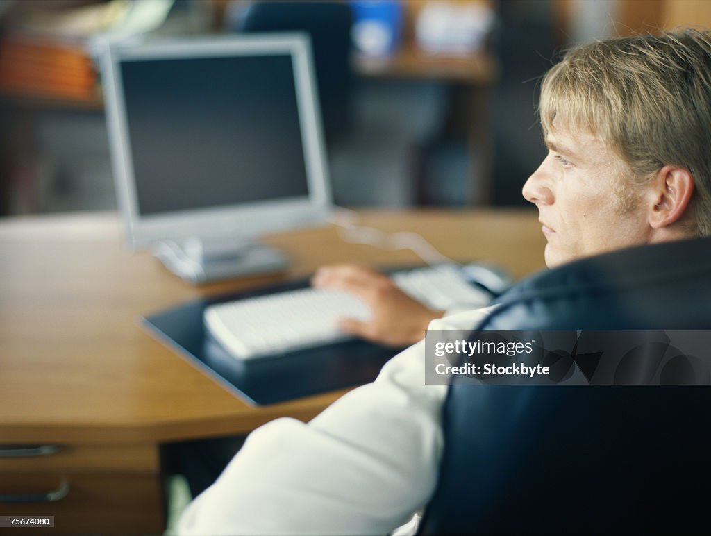 Man sitting in office with computer, looking away