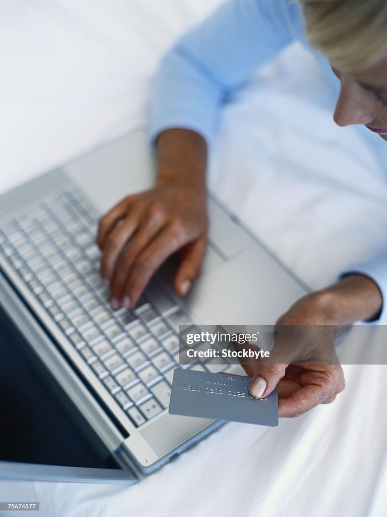 Woman using laptop, holding credit card, elevated view