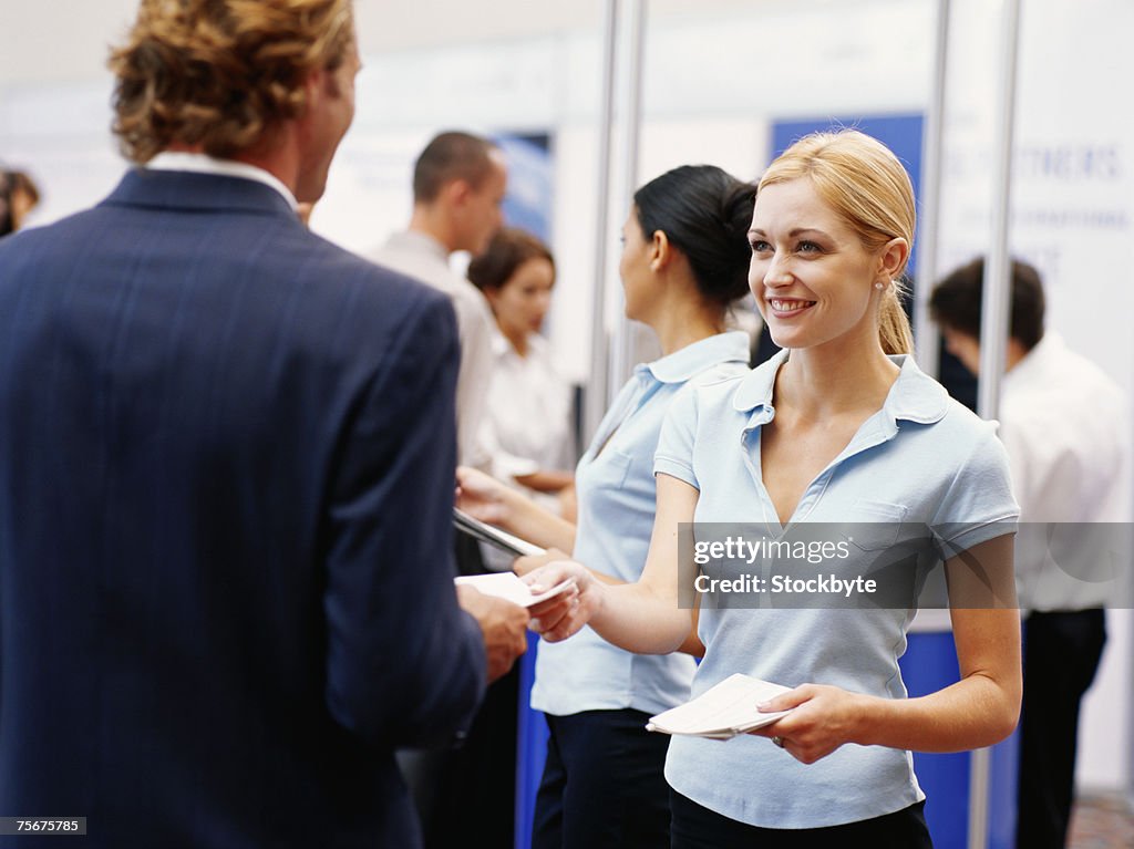 Sales executive giving brochures to businessman at exhibition