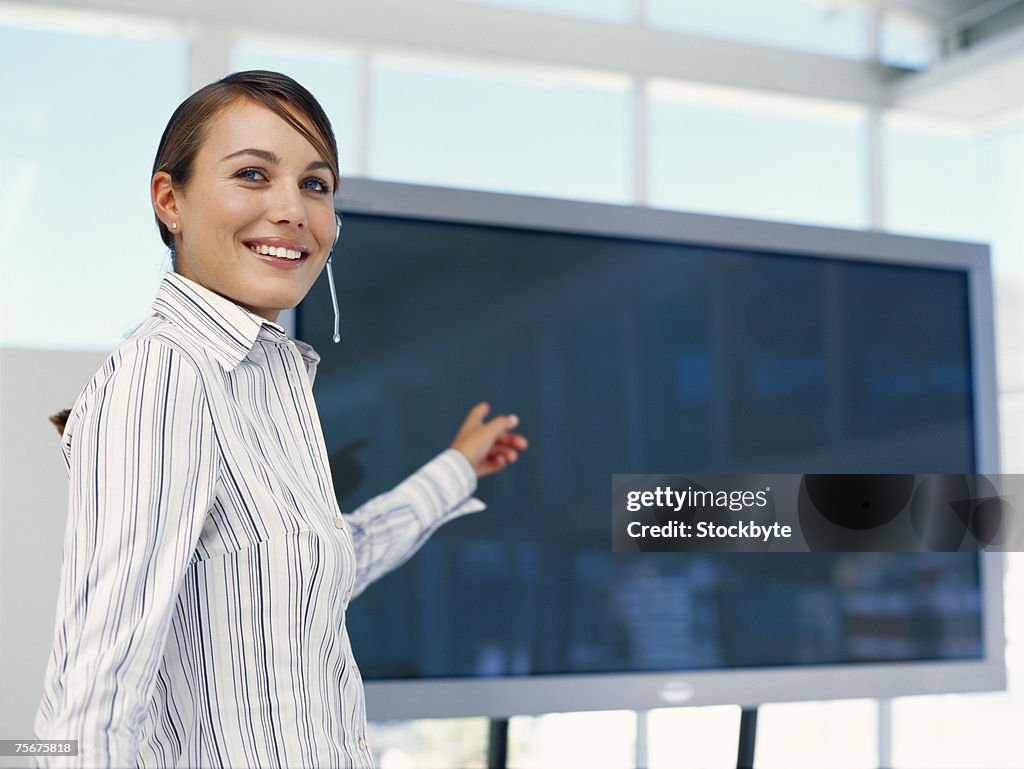 Businesswoman giving presentation at seminar, pointing at flat screen, side view