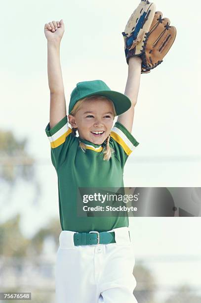 girl (6-7) wearing baseball glove cheering, arms up, smiling - girl baseball cap stock pictures, royalty-free photos & images