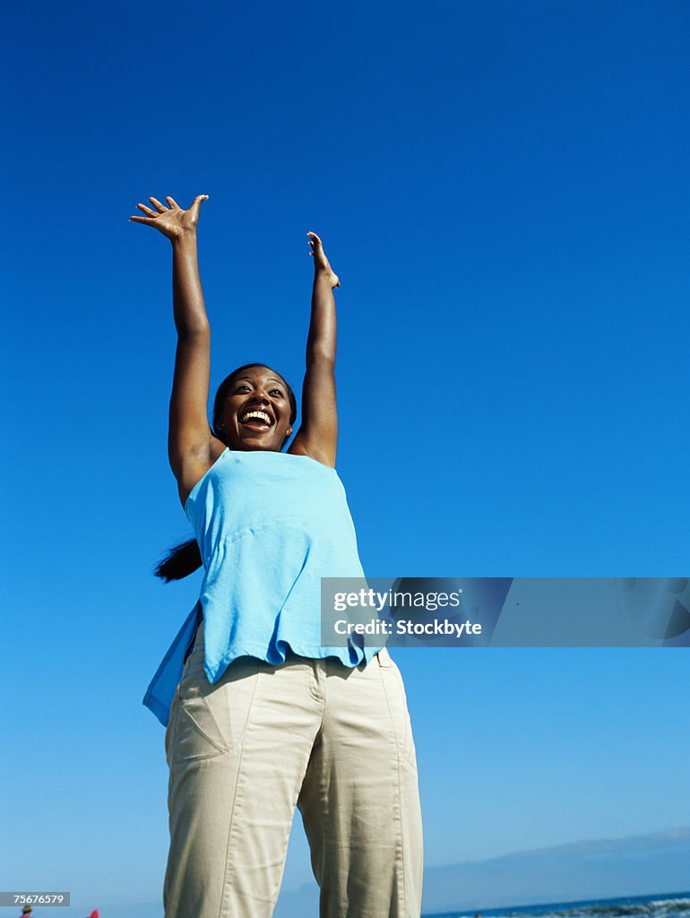 Young woman raising hands, smiling, low angle view