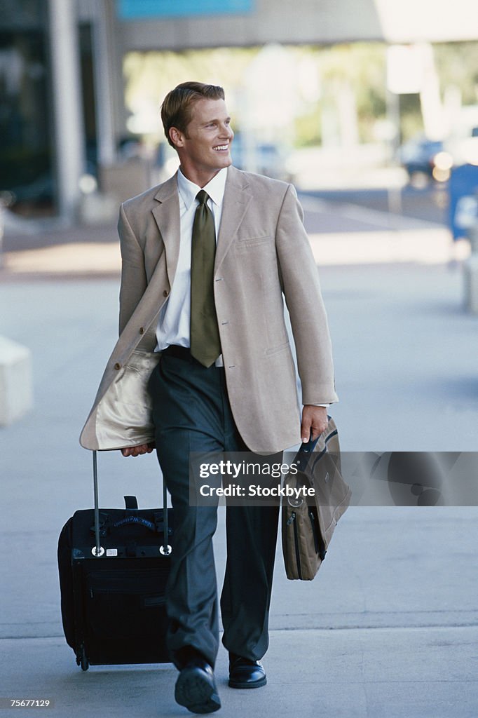 Businessman walking in airport with luggage, looking away