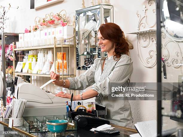 young woman, sales clerk in gift shop, using cash register, smiling, side view - gift shop interior stock pictures, royalty-free photos & images
