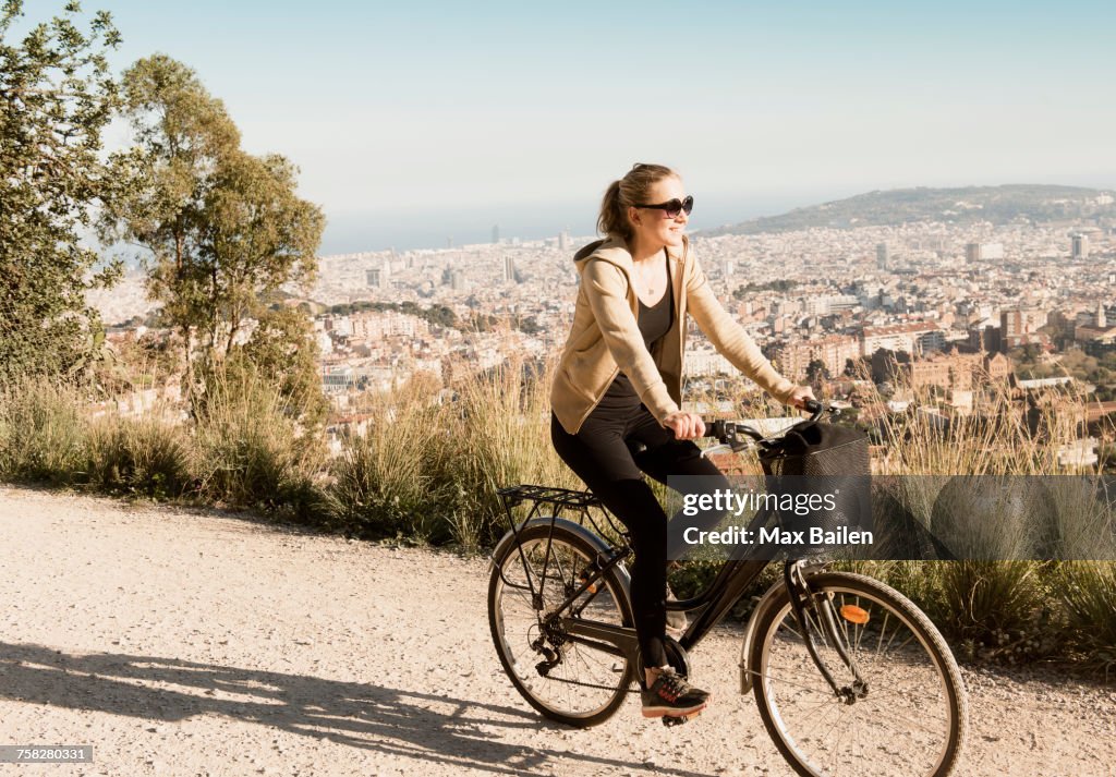 Woman sightseeing on bicycle, city in background, Barcelona, Catalonia, Spain
